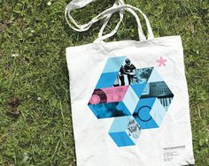 a white bag sitting on top of a lush green field next to a blue and pink geometric design