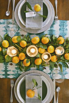 the table is set with plates, silverware and oranges on them for an elegant dinner