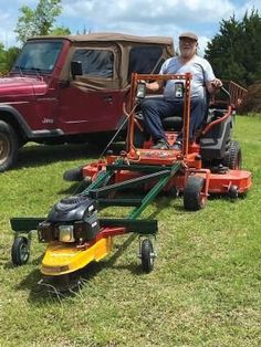 a man riding on the back of a lawn mower next to a red truck