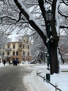 people walking down a snowy street in front of a large building with lots of snow on the ground