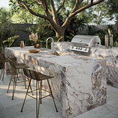 an outdoor kitchen with marble counter tops and bar stools next to the grill area