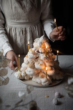 a woman is decorating a cake with white flowers and lit candles on the table