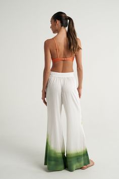 The SIGAL High Waisted Flared pants are a relaxed yet sophisticated resort wear piece. High waisted and wide bottom leg. Flat high waistband in front, gathered with encased elastic at the Back. Wide band cuff at bottom. Hand-drawn tropical print placed strategically on the body. Handcrafted in luxurious fabric, with a soft linen weave and effortless viscose drape. Waistband is flat on the front, gathered on the back with elastic. Model is wearing size S. Relaxed Fit. Hand drawn textile design. 8 Beach Season Wide Leg Harem Pants With Elastic Waistband, Wide Leg Harem Pants With Elastic Waistband For Beach, White Pants With Elastic Waistband And Tie-side, White Bottoms With Gathered Waist For Summer, Summer Vacation Bottoms With Gathered Waist, Vacation Wide Leg Harem Pants With Elastic Waistband, Summer Wide Leg Pants With Elastic Waistband, Wide Leg Harem Pants With Elastic Waistband For Vacation, Summer Pants With Gathered Waist And Loose Hips