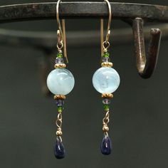 "Moss Aquamarine and natural Blue Sapphire Earrings A natural dark blue Sapphire Briolettes are dangling below large (10mm) Blue Moss Aquamarine beads accented with green Diopside and Iolite beads. The Briolette and the gems are wrapped with high quality 14k gold filled wire and swing from a gold filled hook. These are natural, not colourd excellent AAA quality gems, beautifuly faceted and sparkling. An elegant and feminine, chic statement earrings, perfect for special occasion, wedding, holiday Blue Drop Jewelry With Natural Stones, Blue Gemstone Drop Earrings, Blue Dangle Jewelry With Gemstone Accents, Blue Long Drop Jewelry With Natural Stones, Blue Briolette Jewelry With Matching Earrings, Elegant Sapphire Earrings With Natural Stones, Blue Aquamarine Drop Jewelry, Blue Natural Stones Long Drop Jewelry, Aquamarine Drop Earrings