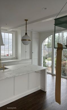 an empty kitchen with white cabinets and marble counter tops in front of large open windows