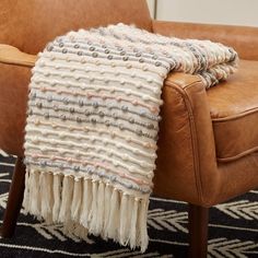 a brown chair with a blanket on top of it next to a tan leather chair