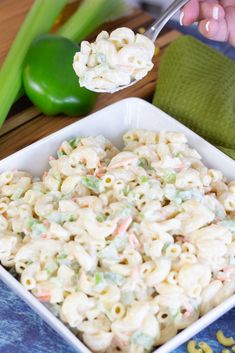 a spoon full of macaroni salad on a white plate next to green peppers