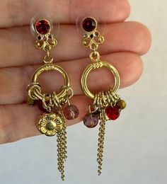 Beautiful gold toned metal, with a ruby red crystal on the front of the post.  They are about 2 1/2 inches long with multicolored, faceted beads and a gold sunflower hanging from a ring.  Fun with a lot of movement and sparkle. Jeweled Metal Dangle Crystal Earrings, Gold Metal Chandelier Earrings With Dangling Charms, Red Jeweled Metal Earrings, Bohemian Gold Faceted Earrings, Gold Faceted Chandelier Dangle Earrings, Gold Faceted Dangle Chandelier Earrings, Gold Faceted Dangle Crystal Earrings, Gold Ornate Chandelier Earrings, Gold Teardrop Chandelier Clip-on Earrings