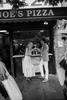 a man and woman are standing in front of a pizza shop talking to each other