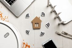 a table topped with smart devices next to a laptop computer and a house shaped cutout