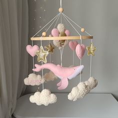 a pink and white dolphin mobile hanging from a wooden rod with stars, clouds, and hearts