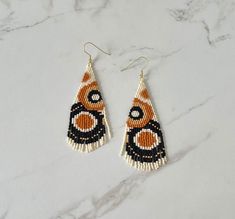 two pairs of beaded earrings on top of a marble counter with white and orange beads