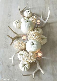 a table topped with white pumpkins and antlers next to candles on top of a wooden floor