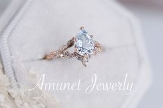 an engagement ring with a blue topaz surrounded by white feathers and the words annnet jewelry