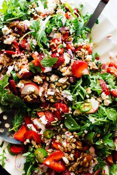 a salad with strawberries and nuts is on a white plate next to a fork