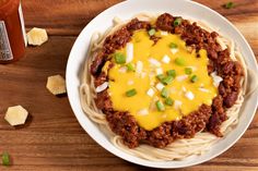 a white plate topped with chili cheese and noodles next to a jar of ketchup