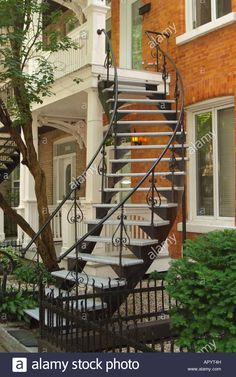 a wrought iron spiral staircase in front of a brick building with trees and bushes on the sidewalk