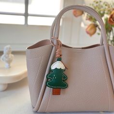 a handbag with a christmas tree on the front and small keychain attached to it