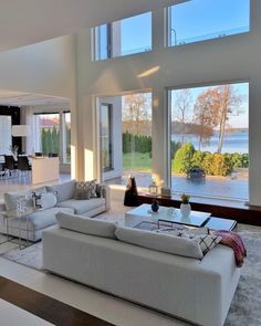 a living room filled with white furniture and large windows overlooking the water's edge