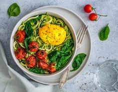 a white bowl filled with pasta, tomatoes and spinach on top of a table