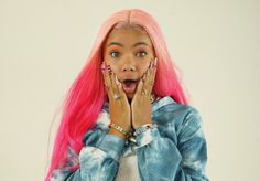 a woman with pink hair making a surprised face while holding her hands to her mouth