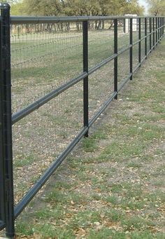 a black metal fence with grass and trees in the background