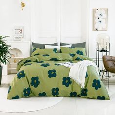 a bed with green flowers on it in a room next to a chair and potted plant