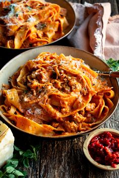 two bowls filled with pasta and sauce on top of a wooden table