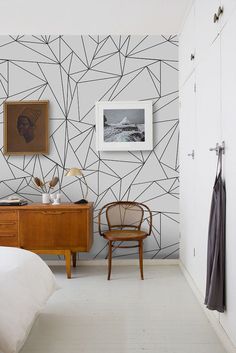 a bedroom with a bed, desk and chair in front of a geometric wallpaper