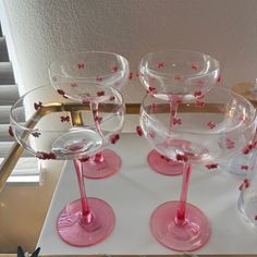 four wine glasses sitting on top of a white table with pink rims and red flowers