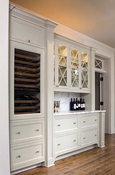 an empty kitchen with white cabinets and wood flooring, along with wine bottles on the shelves