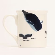 a coffee cup with a whale painted on the front and side, sitting on a white surface