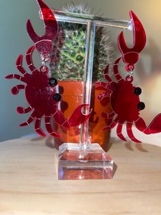 the red seahorse earrings are on display next to a cactus in a glass vase