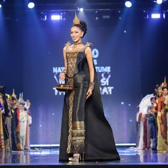 a woman is walking down the runway in a black and gold dress with an elaborate crown on her head