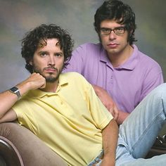 two men sitting next to each other in front of a gray background, one with his hand on his chin