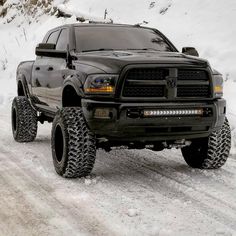 a large black truck driving down a snow covered road