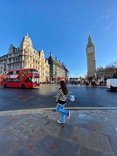 a woman is walking down the street in front of big ben and red double decker bus