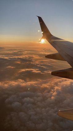 an airplane wing flying over the clouds at sunset