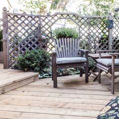 two chairs sitting on a wooden deck next to a planter and trellis fence