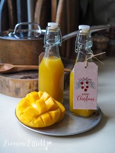 two glass bottles filled with orange juice next to a sliced mango on a plate and another bottle full of orange juice