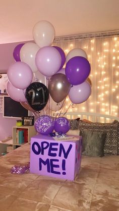 an open me box with balloons and streamers