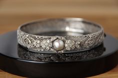 This is a stunning art deco style silver filigree clasp bracelet bangle, with cultured pearl (not tested) and with quartz or paste diamonds, engraved STERLING on the inside. One stone is missing from the front setting and there is some wear and slight bend to the shape of the bangle, please review photos thoroughly to see condition! The clasp with slide opening is in good working order and the filigree is in good condition.  Band width: 10mm Internal circumference: approx. 17.75cm All informatio Silver Filigree Bangle For Gift, Victorian Style Silver Engraved Bangle, Ceremonial Silver Filigree Bangle, Vintage Engraved Antique Silver Bangle, Vintage Etched Sterling Silver Bangle Bracelet, Sterling Silver Filigree, Bracelet Clasps, Silver Gifts, Silver Filigree