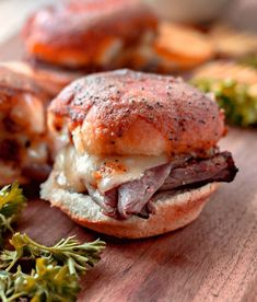 roast beef and swiss cheese sliders on a wooden cutting board with herbs next to them