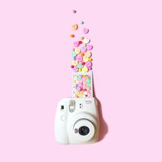 a camera with candy sprinkles coming out of it on a pink background