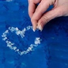 someone is making a heart out of snow flakes on a sheet of blue paper