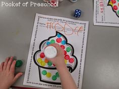 a child's hand is playing with colored dices on the table next to a coloring book