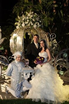 a bride and groom posing for a photo in front of a carriage with flowers on it