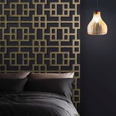 a bed sitting under a lamp next to a wall with a black and gold pattern on it