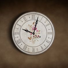 a white clock with flowers painted on it's face and numbers in roman numerals