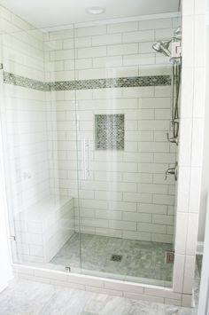 a walk in shower sitting next to a white tiled wall and floor with a glass door